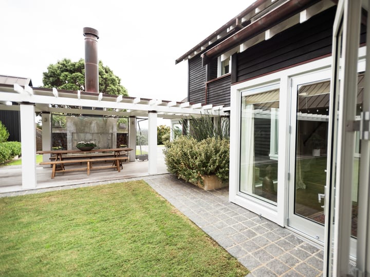 Dark-clad exterior with white pergola, glass doors, stone tile path, and lawn