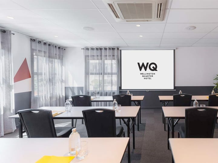 White-walled meeting room with black chairs, white tables, projection screen, and coloured wall feature