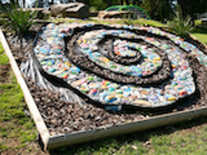 Painted-stone spiral garden feature with children seated beside it