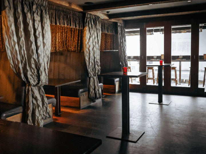 Darkened bar interior with draped fabric booth dividers, chandelier, and high stools along tall tables