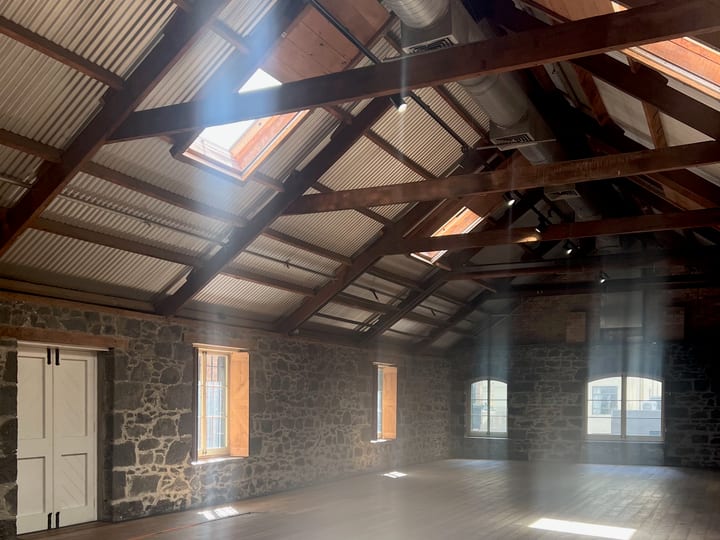 Empty stone-walled barn with exposed timber beams, skylights, and timber floor