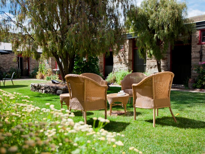 Sunny courtyard with wicker chairs on a lawn and historic schist-stone buildings with red window frames