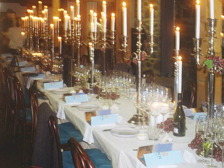 Long white-linen dining table with candelabras and glassware under exposed timber beam ceiling