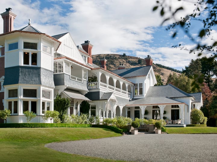 Large Victorian timber mansion with bay tower, wraparound veranda, slate roof, and manicured lawn and gravel drive
