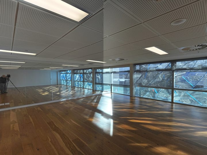 Empty dance or function room with polished timber floor, full-length mirrors, and large glazed panels with blue artwork