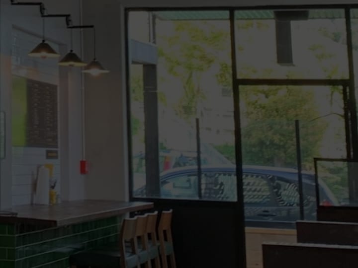 Cafe counter area with green tiled front, shelving, pendant lights, and large windows
