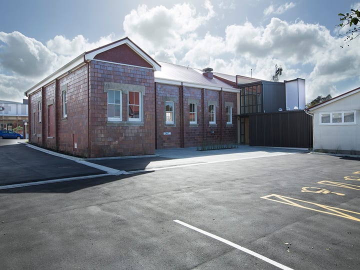 Red-brick hall with white trim and metal extension, viewed from car park
