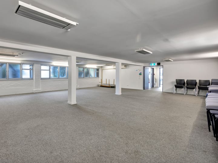 Plain carpeted room with columns and stacked chairs along the wall