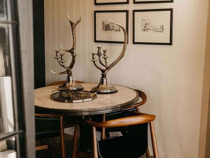 Dining corner with a round marble-top table, mid-century chairs and framed sketches on white timber walls