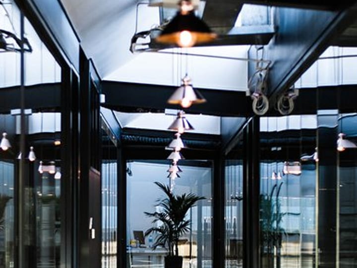 Narrow glass-walled corridor with pendant lights and polished floor, opening to a workspace