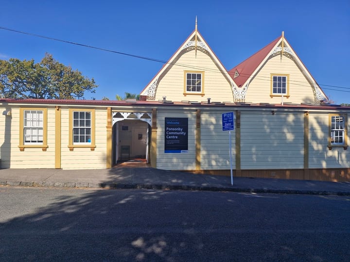 Cream weatherboard heritage hall with decorative gable trim, red roof and arched vehicle entrance