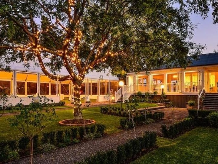 Estate homestead at dusk with fairy-lit trees and illuminated marquee