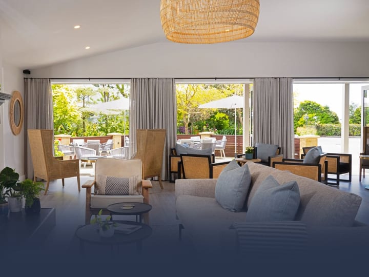 Lounge interior with fireplace, neutral sofas, woven pendant light, and open bifold doors to a terrace
