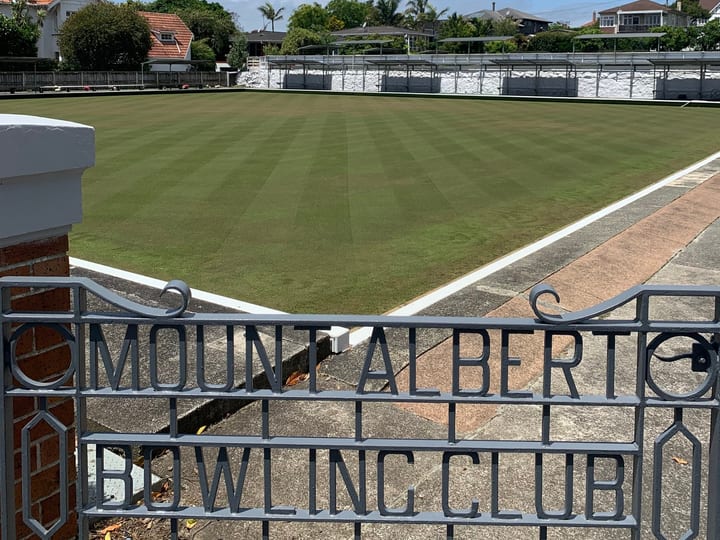 Bowling green and surrounds viewed through ornate metal gates with club name