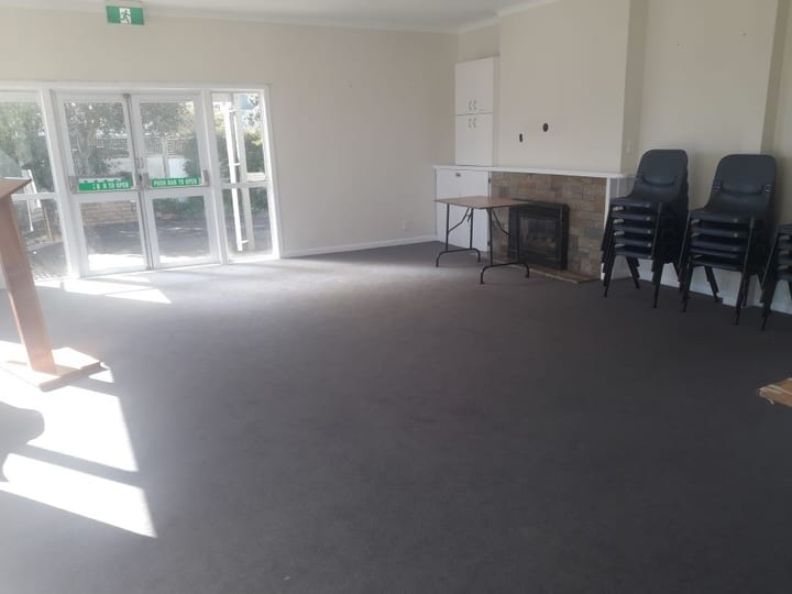 Open room with dark carpet, stacked chairs and fireplace