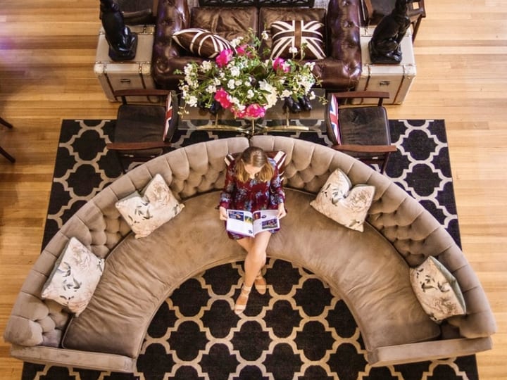 Curved tufted sofa and leather chesterfield on patterned rug, timber floor, overhead view