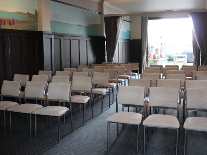 Function room with rows of upholstered chairs, dark timber wall panelling, landscape paintings