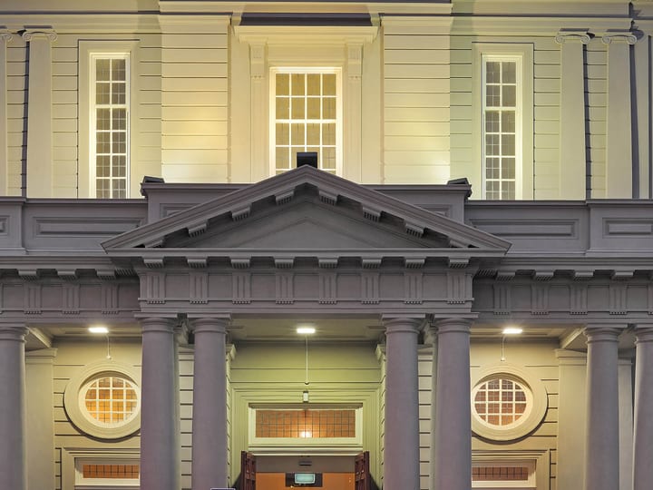 Classical portico facade with columns, triangular pediment, and round windows lit at night