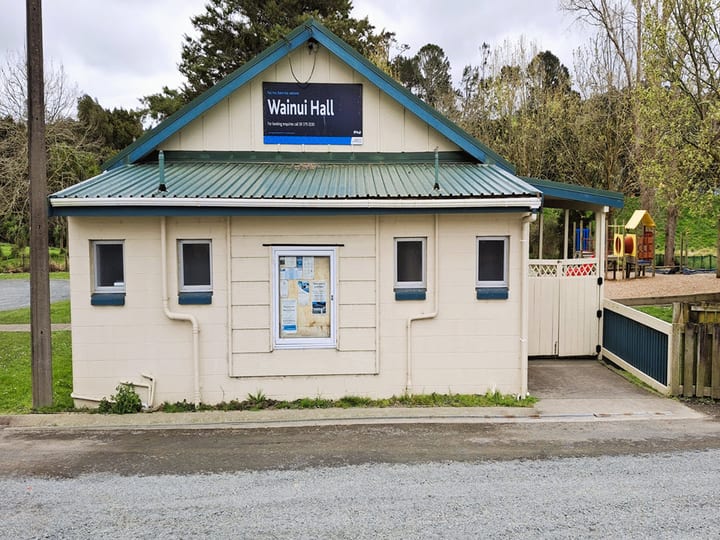 Front elevation of small cream weatherboard hall with green metal roof and signage