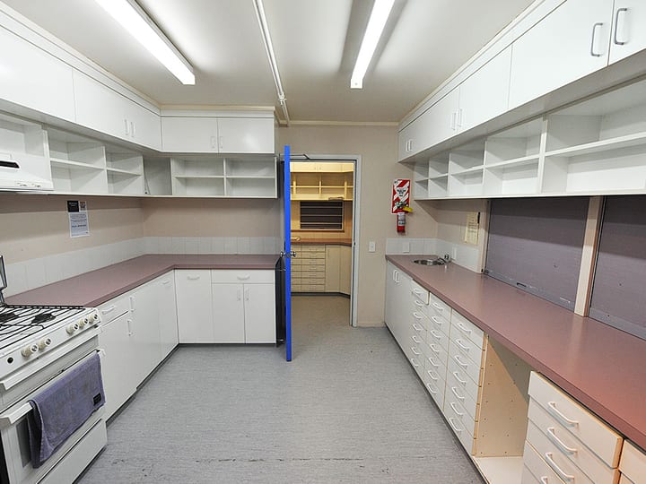 Narrow kitchen with white cabinetry both sides, gas range, and fire extinguisher on wall