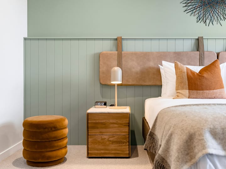 Bedroom with panelled wall, upholstered bedhead and warm-toned furnishings