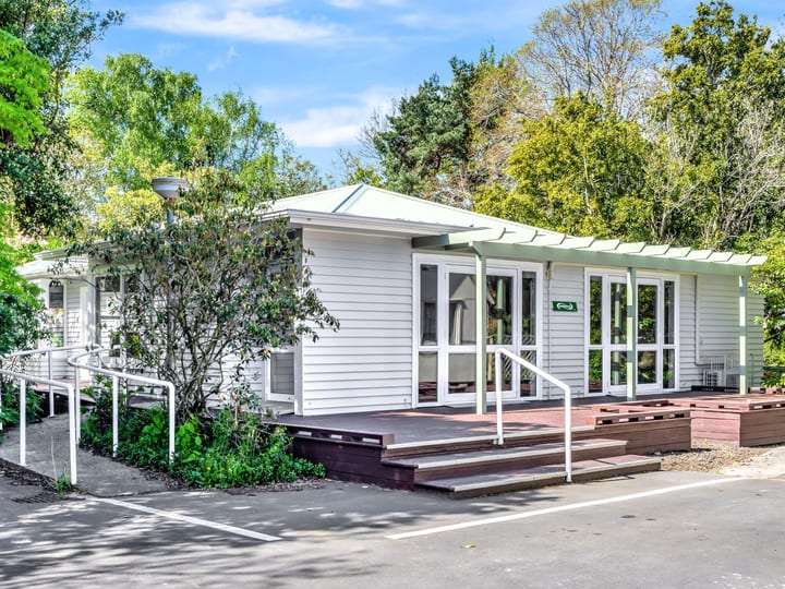 Single-storey weatherboard building with timber deck and ramp entrance surrounded by trees