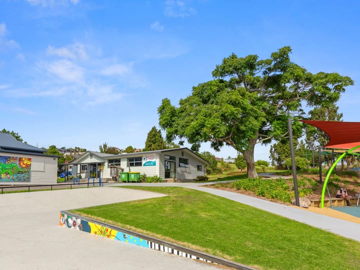 Single-storey community building and playground area with trees and shade sail