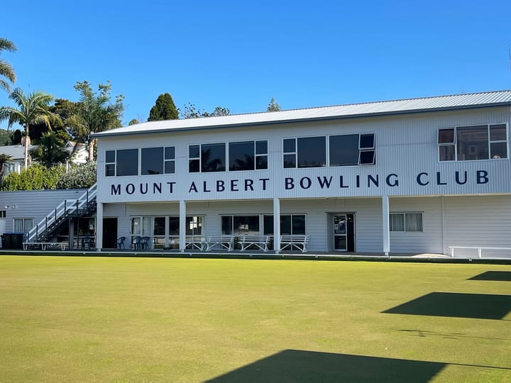 Two-storey white club building beside a flat bowling green