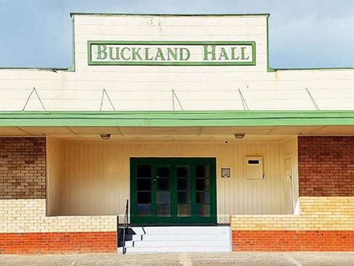 Cream and red brick hall exterior with green-trimmed entrance canopy and signage above double doors