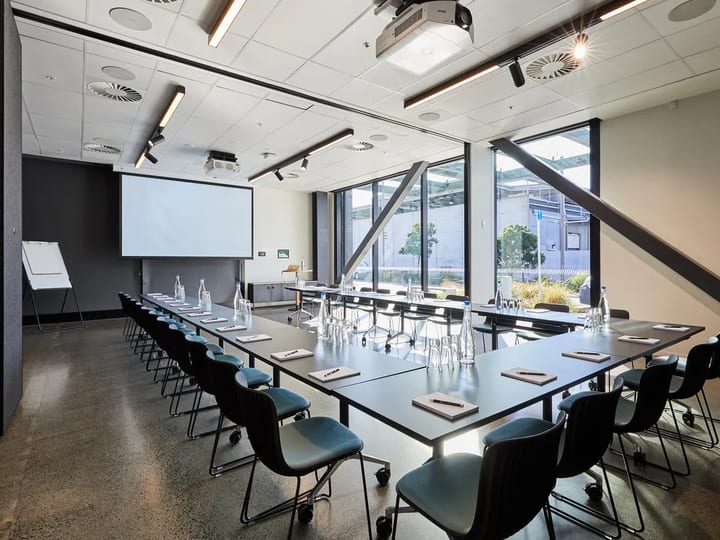 Conference room with U-shaped table arrangement, projector screen, and exposed diagonal steelwork