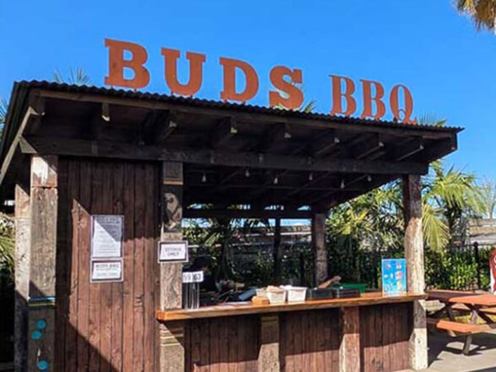 Outdoor rustic bar kiosk with Buds BBQ signage and picnic seating