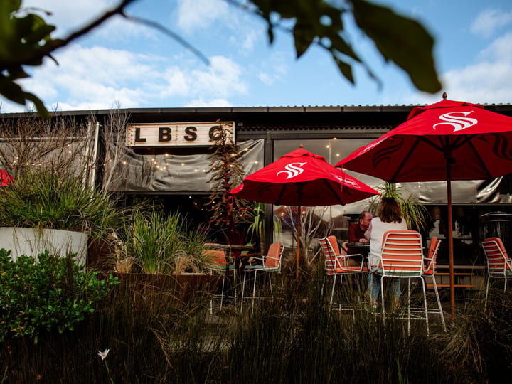 Surf club exterior with outdoor seating, red umbrellas and signage
