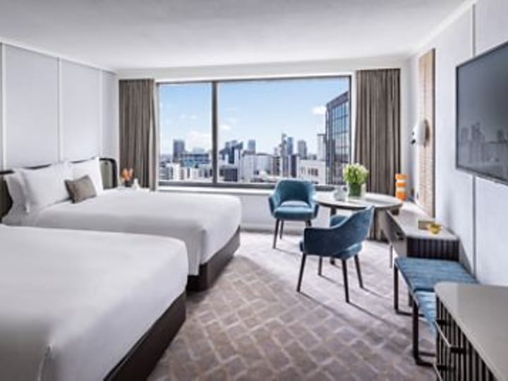 Hotel twin room with two double beds, blue accent chairs, large window with city skyline view