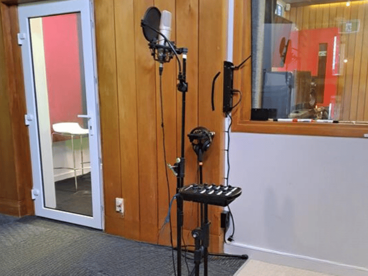 Recording booth with microphone stand, pop filter, and view into control room
