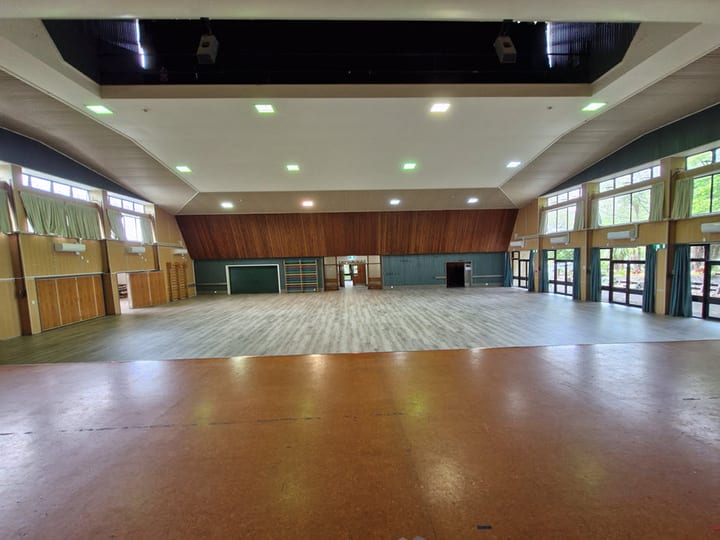 Large open hall with timber wall panels, sports equipment stored along walls