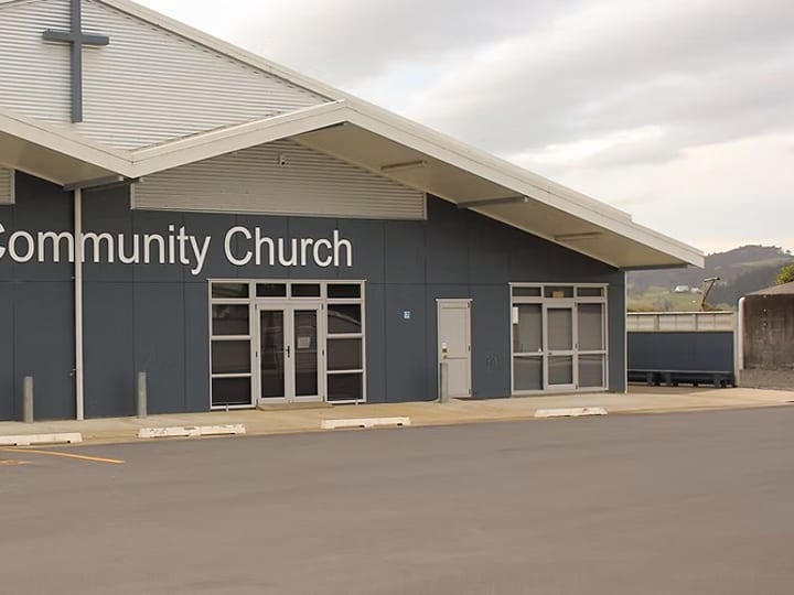 White timber church with pointed gothic window and red roof, driveway entry with signage