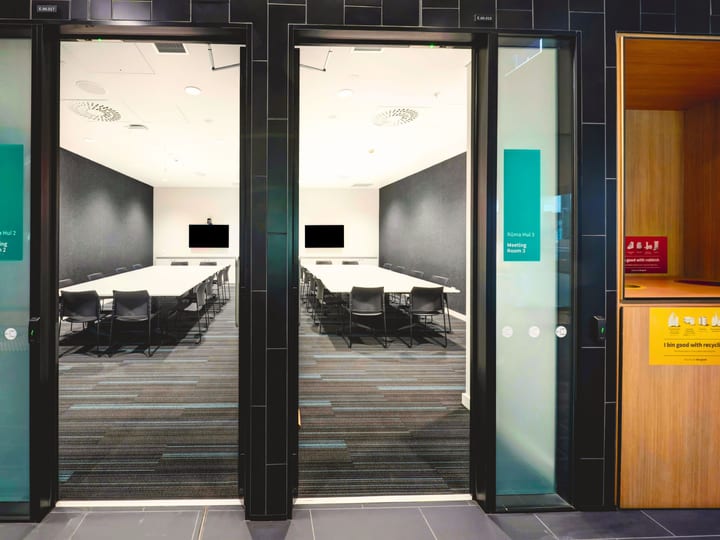 Two adjacent meeting rooms viewed through glass doors, dark walls and patterned carpet