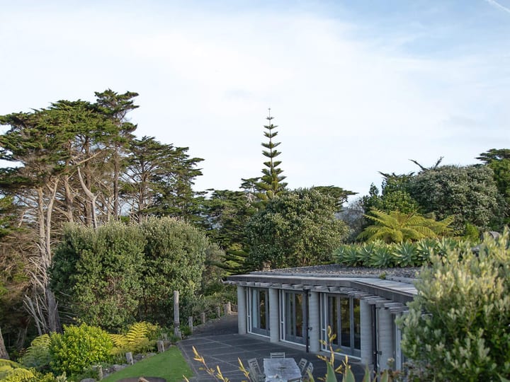 Low curved building with pergola and outdoor dining area set in coastal garden