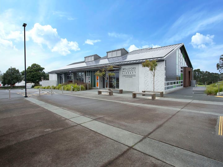 Modern library building with metal roof and decorative panel, car park in foreground