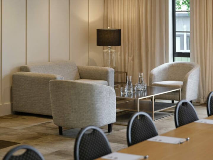 Neutral-toned lounge with two sofas, armchair, floor lamp, and floor-length curtains