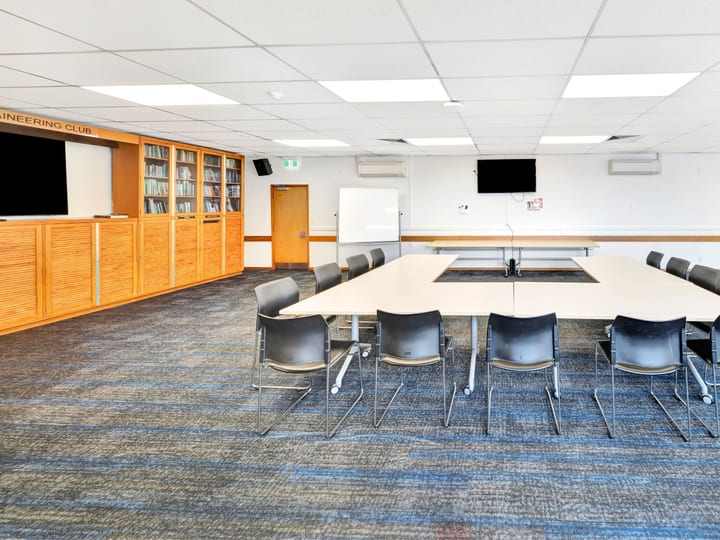 Meeting room with U-shaped table, chairs, bookshelves and wall screens