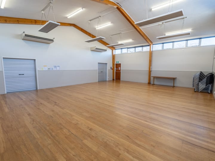 Empty hall with timber floorboards, exposed beam ceiling and roller doors on side wall