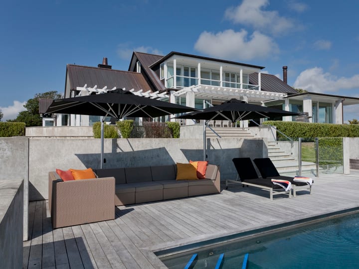White render house with dark roof, pool terrace, deck furniture, and pergola beyond