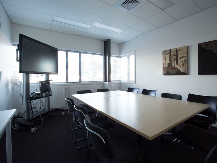 Meeting room with table, chairs, screen and artwork on wall
