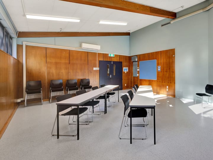 Small meeting room with folding tables, black chairs, timber-panelled wall, whiteboard, and large windows