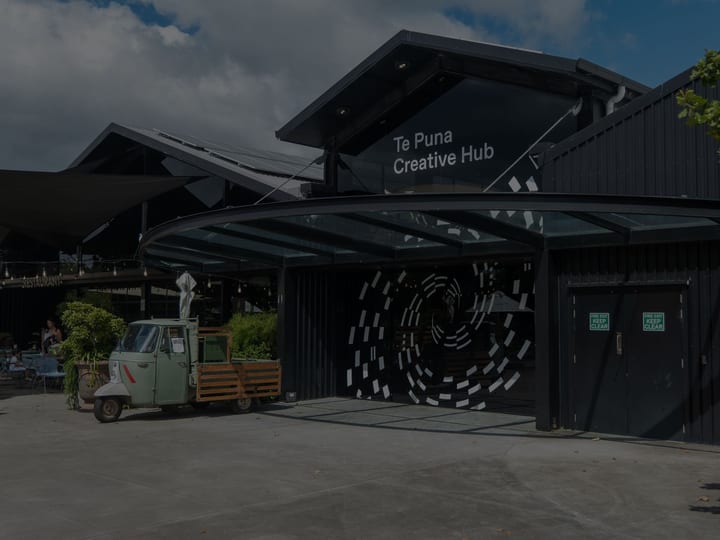 Dark timber-clad building with covered entry, large spiral mural on wall, outdoor courtyard