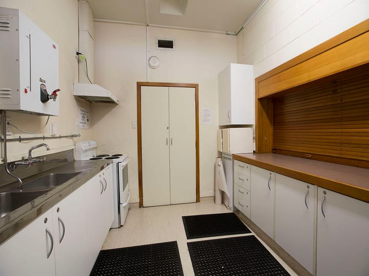 Narrow kitchen with stainless sink, oven, timber cabinetry, and servery counter