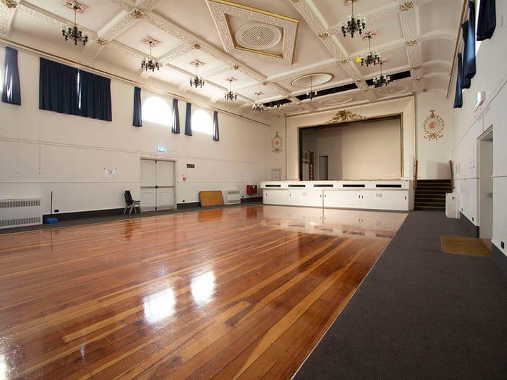 Grand hall facing raised platform, ornate ceiling and polished timber floor