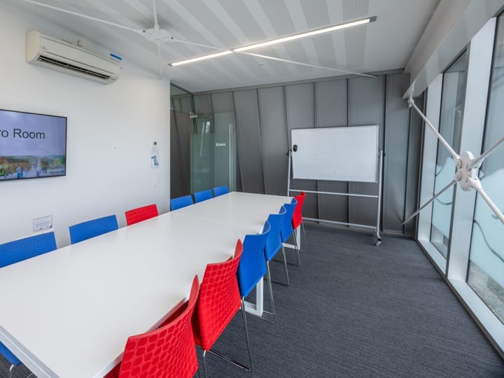 Long meeting room with coloured chairs, whiteboard and wall screen