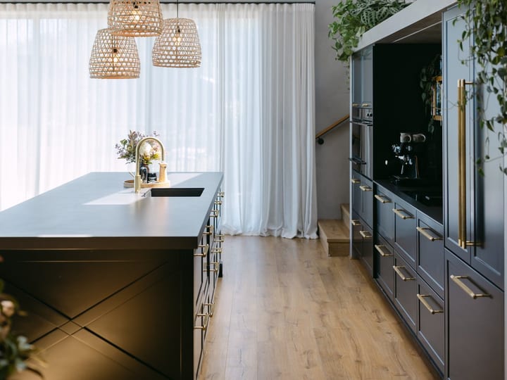 Kitchen with a large island, dark blue cabinetry with brass handles, vaulted ceiling, and woven pendants